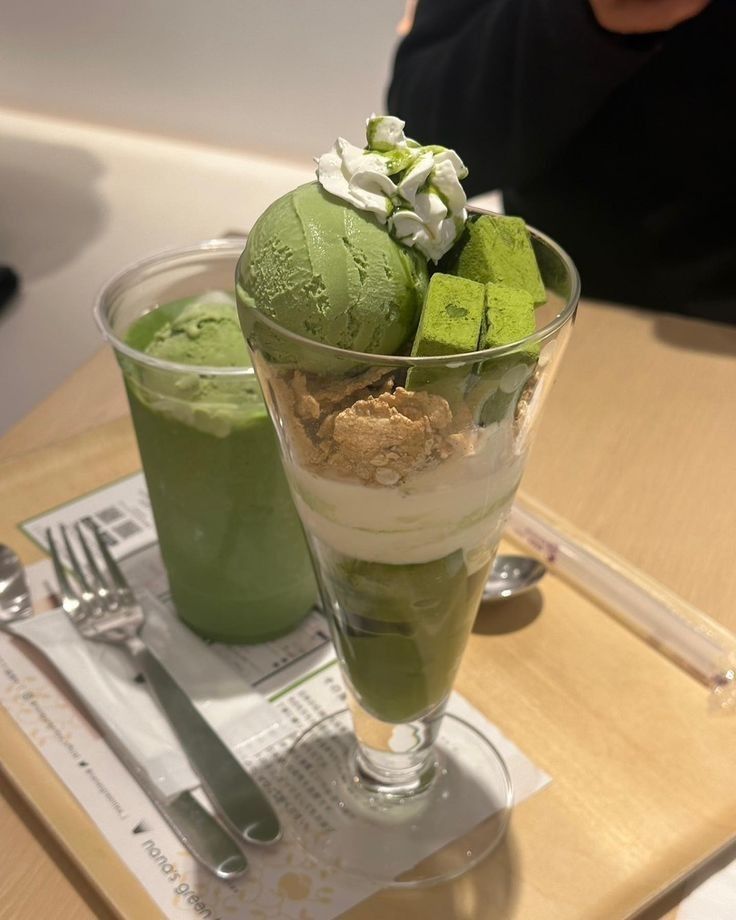 two glasses filled with green dessert on top of a wooden table