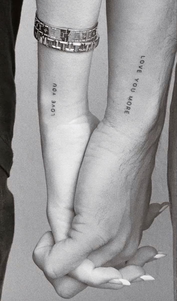 two people are holding hands with tattoos on their arms and one has a heart in the middle