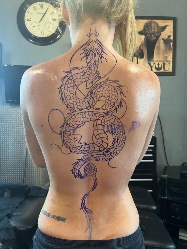 the back of a woman's body with a dragon tattoo on her lower back