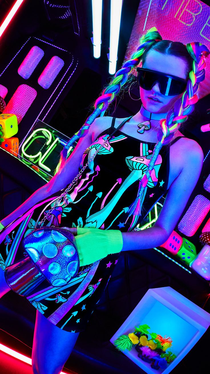 a woman with neon hair and sunglasses is posing in front of some neon colored lights