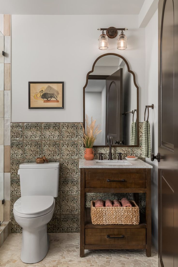 a white toilet sitting next to a bathroom sink under a mirror on top of a wooden cabinet