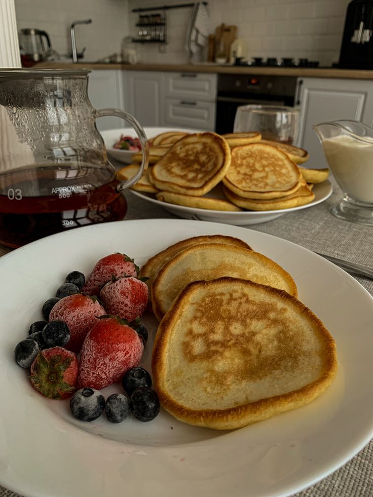 pancakes, strawberries and blueberries on a white plate with syrup in the background