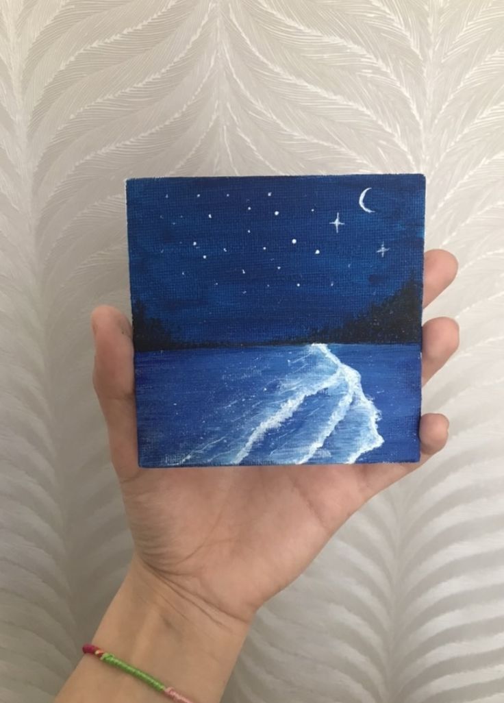 a hand holding up a small piece of art that looks like the ocean at night