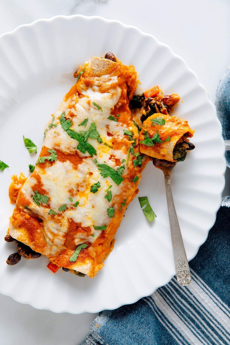 a white plate topped with lasagna covered in cheese and herbs next to a fork