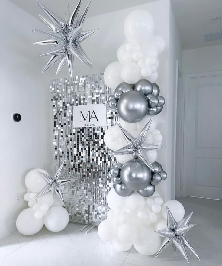 an arrangement of balloons and star decorations in a white room with silver sequins