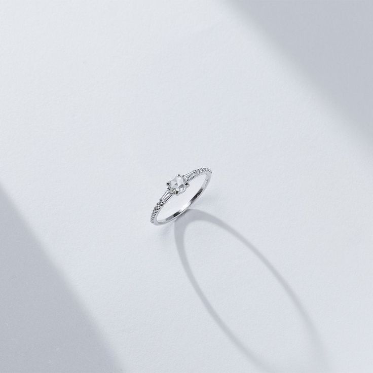 a diamond ring on a white surface with shadow from the light coming in through it