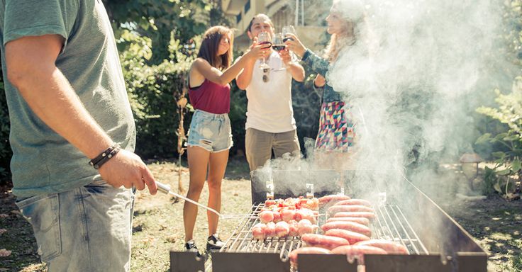 people standing around an outdoor grill with hot dogs and sausages cooking on the grill