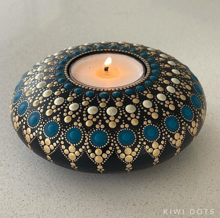 a lit candle sitting on top of a rock covered in blue and gold dots,