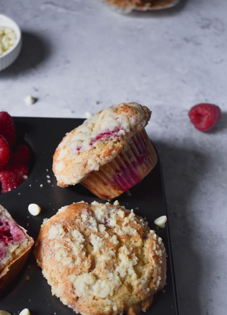 three muffins on a black plate with raspberries and other dessert items