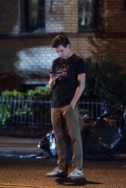 a young man standing in the street looking at his cell phone while wearing a black shirt and khaki pants