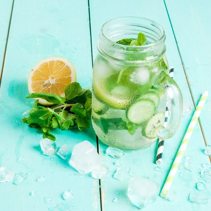 a mason jar filled with cucumber, mint and lemon slices next to two drinking straws