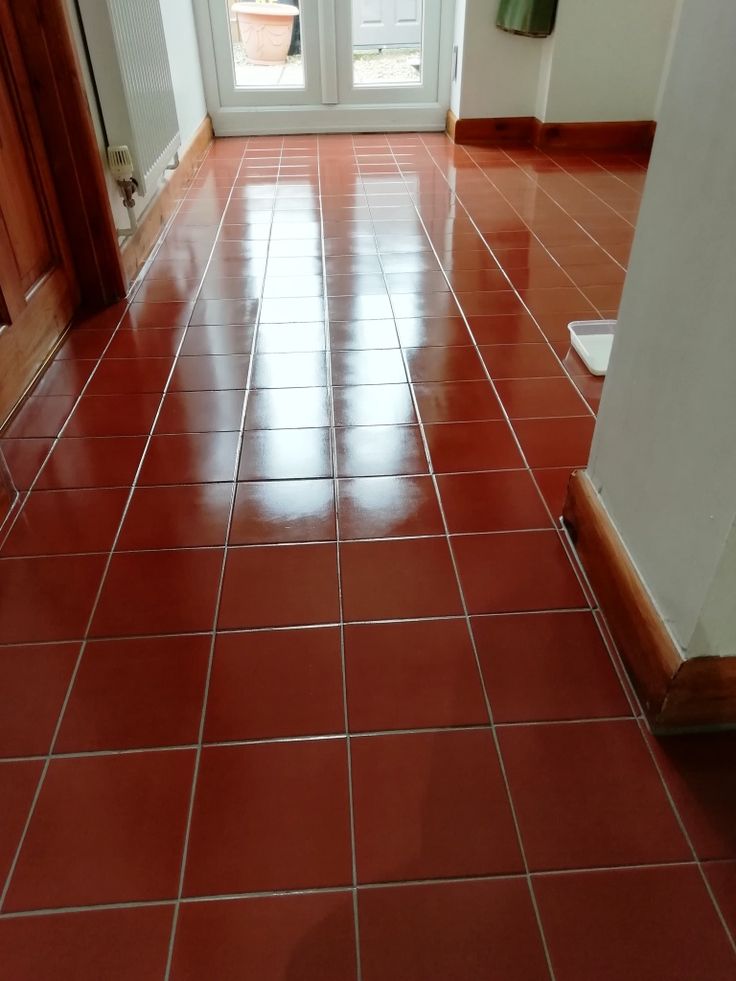 a red tile floor with white trim and door in the background, next to an open doorway