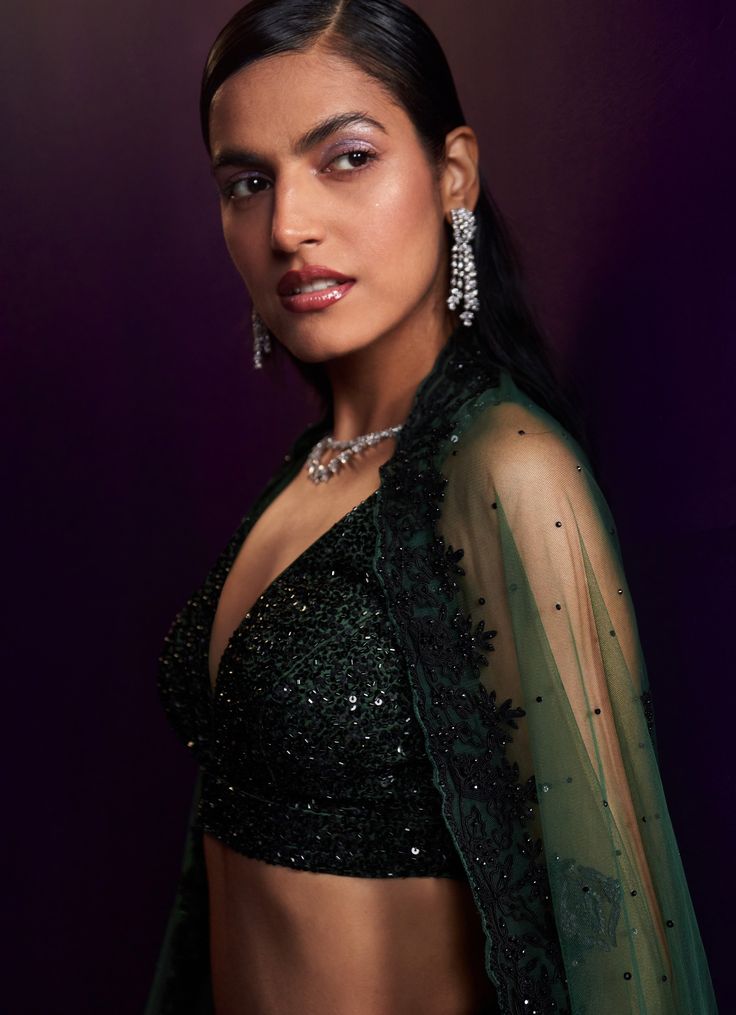 This exquisite Green Embroidered Bridal Lehenga Set is a true masterpiece, designed for those who seek elegance and sophistication. Crafted from luxurious organza fabric, the green lehenga showcases a vibrant green hue, intricately embroidered with contrasting black dori work that creates a captivating interplay of colors. The ensemble is further embellished with black sequins, crystals, and bugle beads, adding a subtle yet glamorous shimmer. Paired with a deep V-neck blouse, this set strikes the perfect balance between traditional charm and modern style. The look is completed with a matching dupatta, adorned with delicate detailing, which adds a touch of grace and refinement. Ideal for brides or brides-to-be at cocktail parties, this lehenga set promises to make a lasting impression with Elegant Green Lehenga With Sheer Dupatta, Elegant Green Lehenga With Resham Embroidery, Green Embroidered Pre-draped Saree For Reception, Green Organza Lehenga For Reception, Festive Green Lehenga With Sheer Dupatta, Elegant Pista Green Organza Choli, Green Embroidered Party Wear Dupatta, Green Pre-draped Saree With Intricate Embroidery For Wedding, Elegant Green Lehenga With Intricate Embroidery