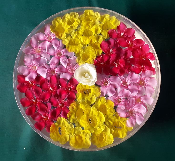 a bowl filled with flowers sitting on top of a green table next to a white flower