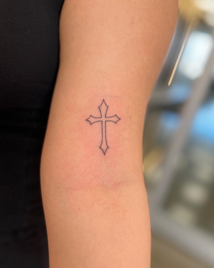 a woman's arm with a cross tattoo on the left side of her arm