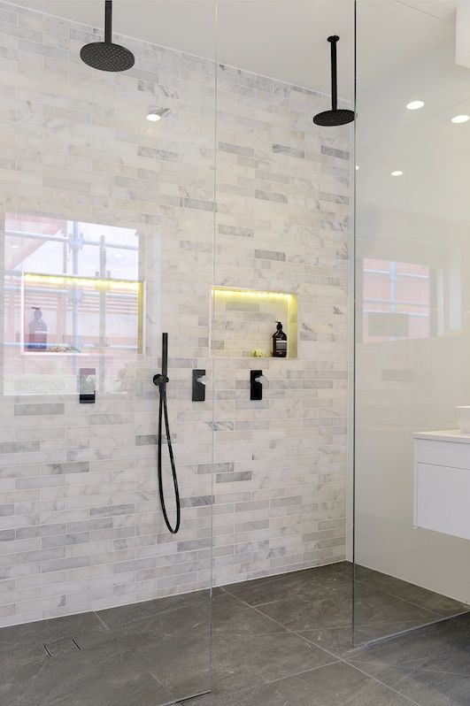 a bathroom with a glass shower door and white marble tiles on the wall, along with a black faucet