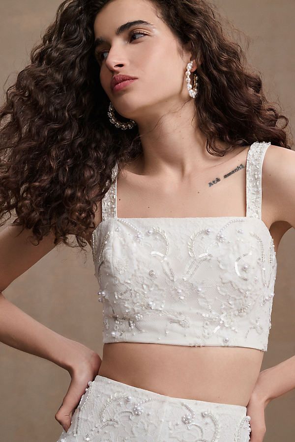 a woman with curly hair wearing a white crop top and high waist skirt, posing for the camera