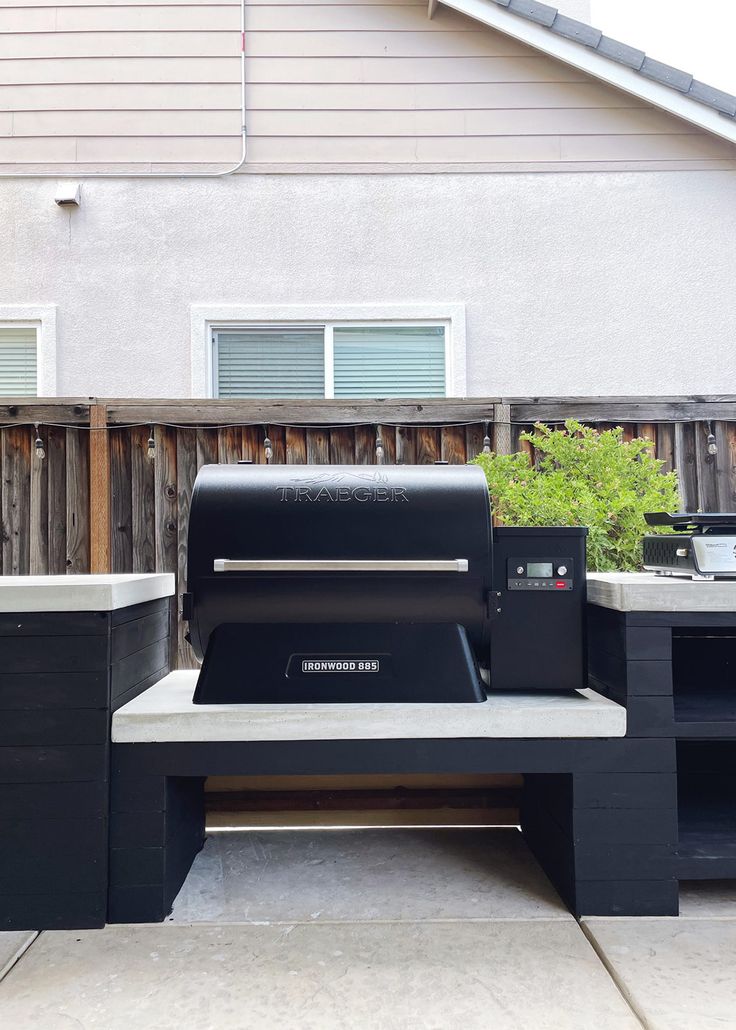 an outdoor bbq grill in front of a house with two black trash bins