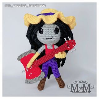 a crochet doll holding a red guitar and wearing a hat with horns on her head