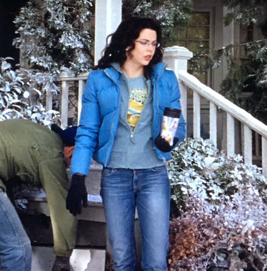 a woman in blue jacket and jeans standing on steps next to snow covered bushes with two men nearby