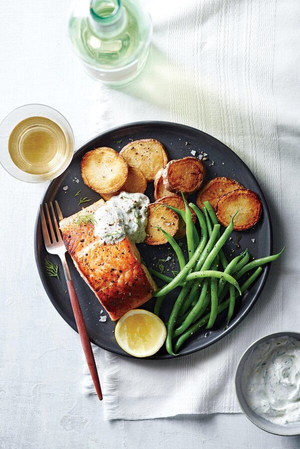 a black plate topped with fish, potatoes and green beans next to a glass of water