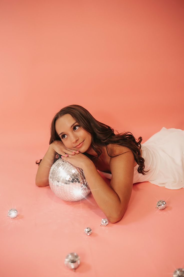 a beautiful young woman laying on the ground next to a disco ball and confetti