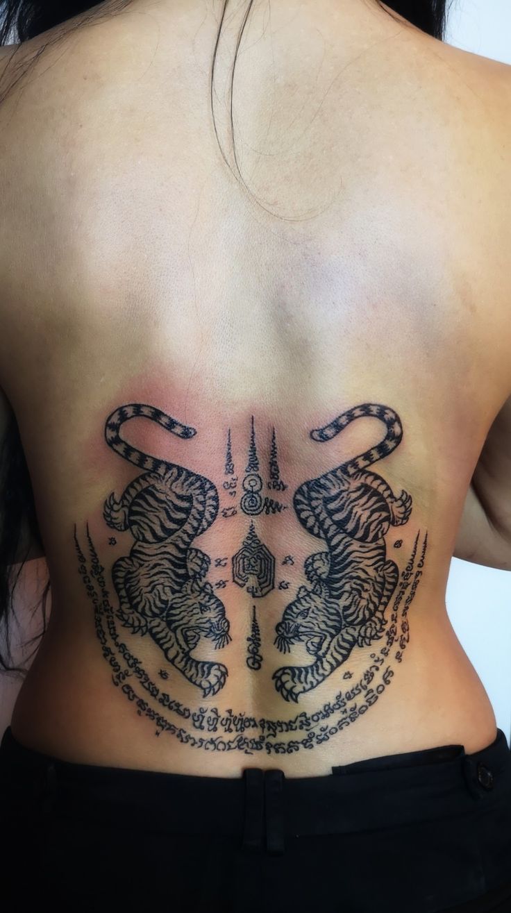 the back of a woman with tattoos on her chest and two tiger heads in chains