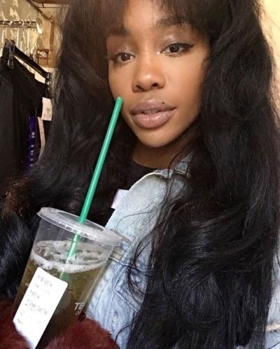 a woman with long hair holding a drink in her hand and looking at the camera