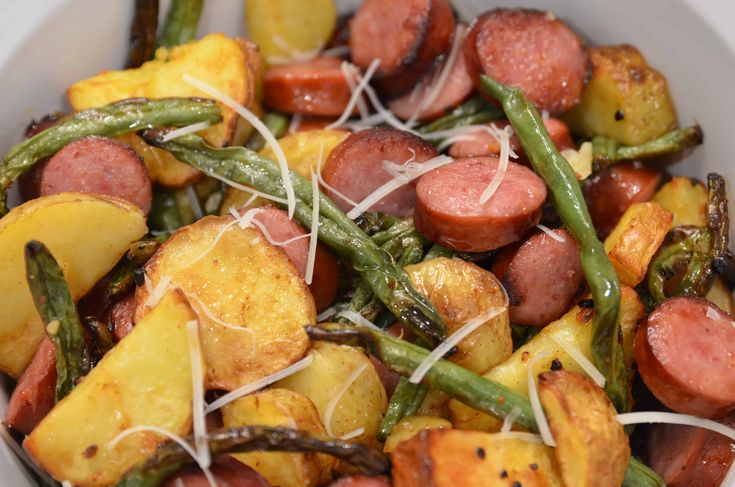 a white bowl filled with potatoes, green beans and sausage on top of string cheese