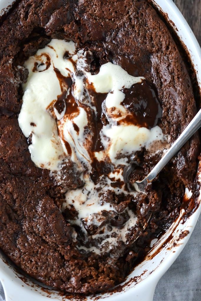 a bowl filled with brownie and ice cream on top of a wooden table next to a spoon