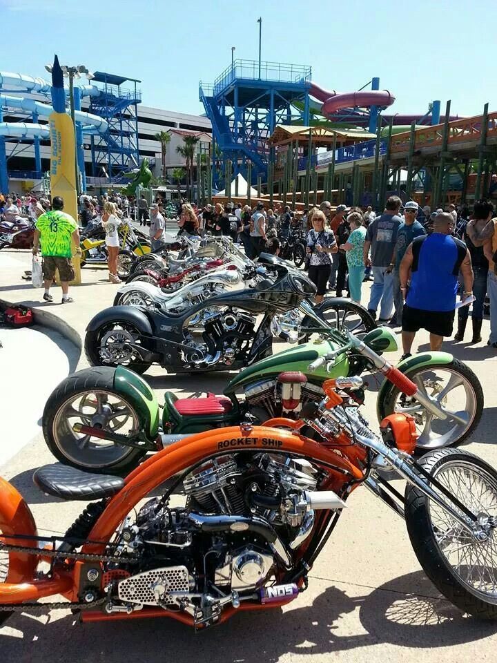 there are many motorcycles that are parked in the parking lot and people standing around them