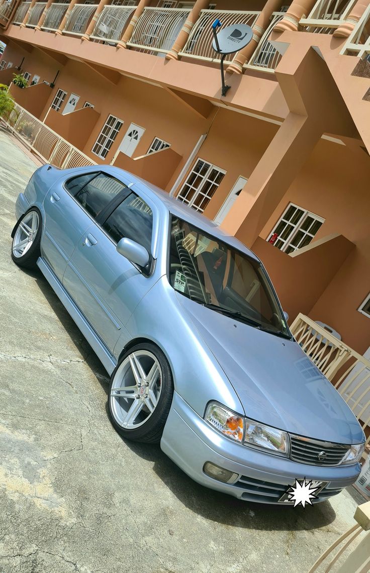 a blue car parked in front of a building with balconies on the side