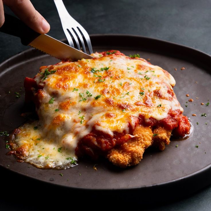 someone is cutting into a piece of chicken parmesan casserole on a plate