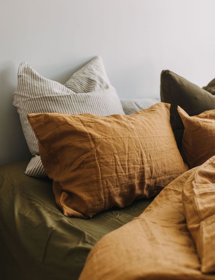 a bed topped with lots of pillows next to a wall