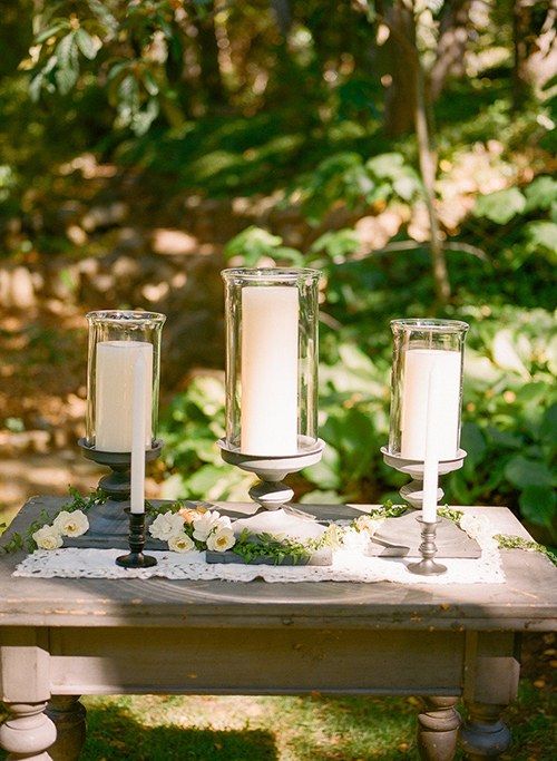 two candles sitting on top of a wooden table with flowers and greenery around it