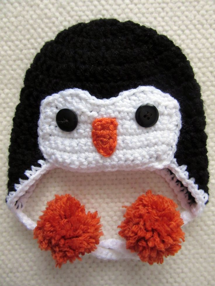 a crocheted penguin hat with orange pom poms