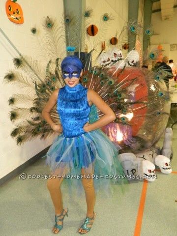 a woman wearing a blue and green costume standing in front of a large fake peacock