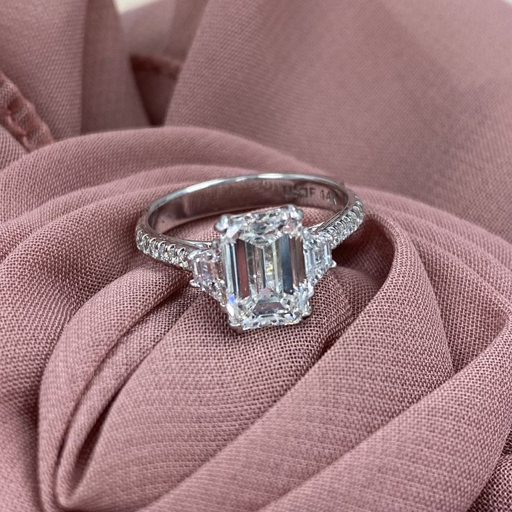 an emerald cut diamond ring on top of a pink fabric