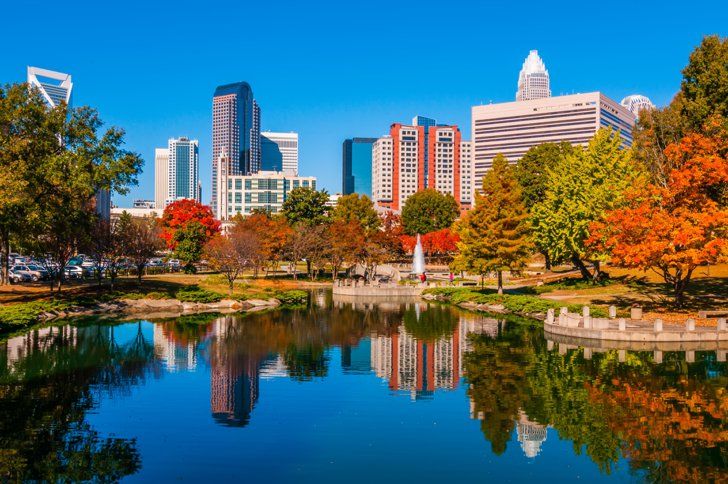 the city skyline is reflected in the still water of a pond on a sunny day