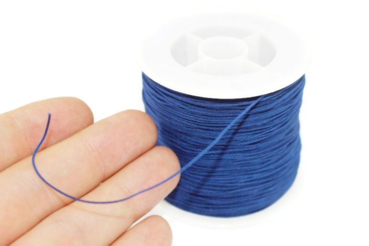 a hand holding a spool of blue thread