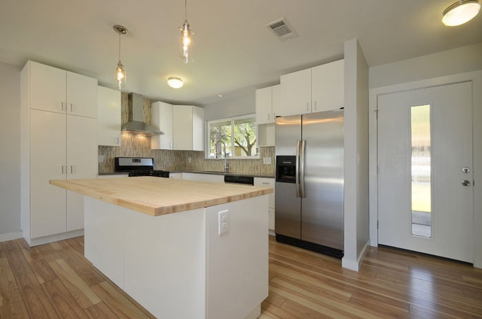 an empty kitchen with white cabinets and wood flooring is pictured in this image, there are lights hanging from the ceiling