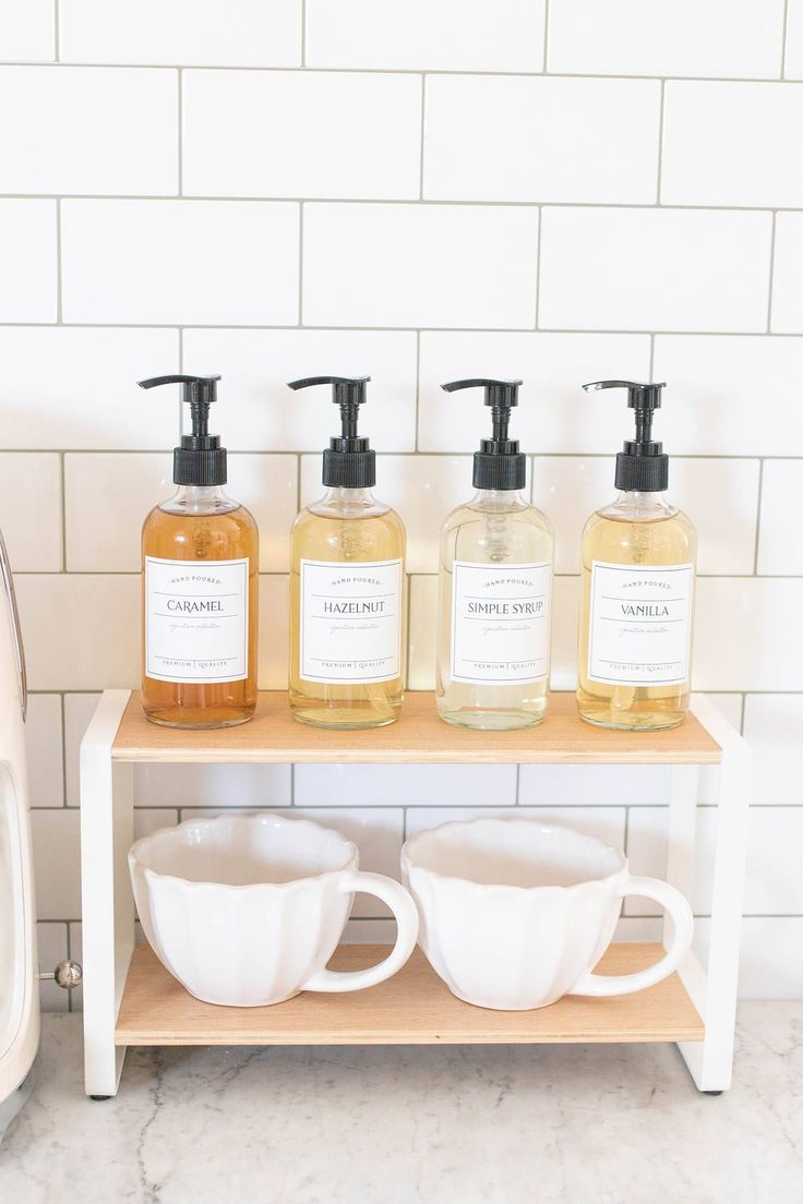 three soap dispensers are sitting on a shelf next to coffee mugs