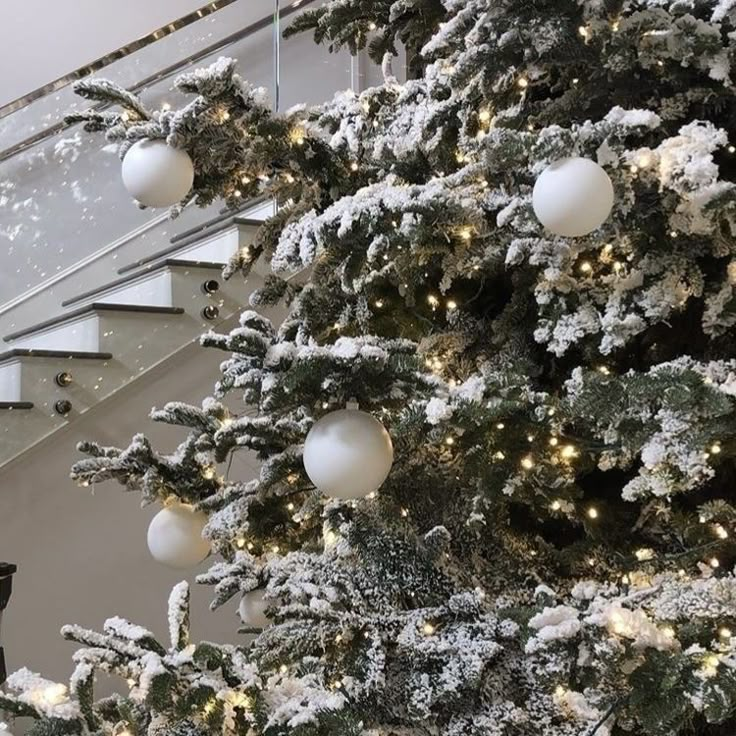 a christmas tree with white balls and snow on it in front of a stair case