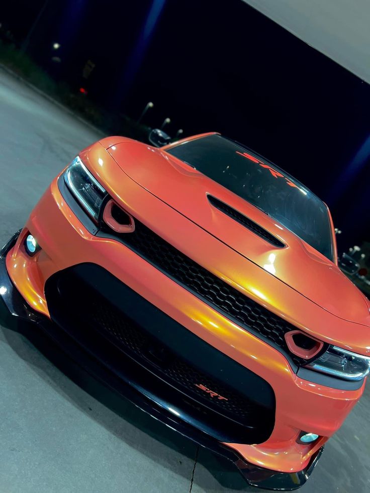 an orange sports car is parked in a parking lot with its hood up and lights on