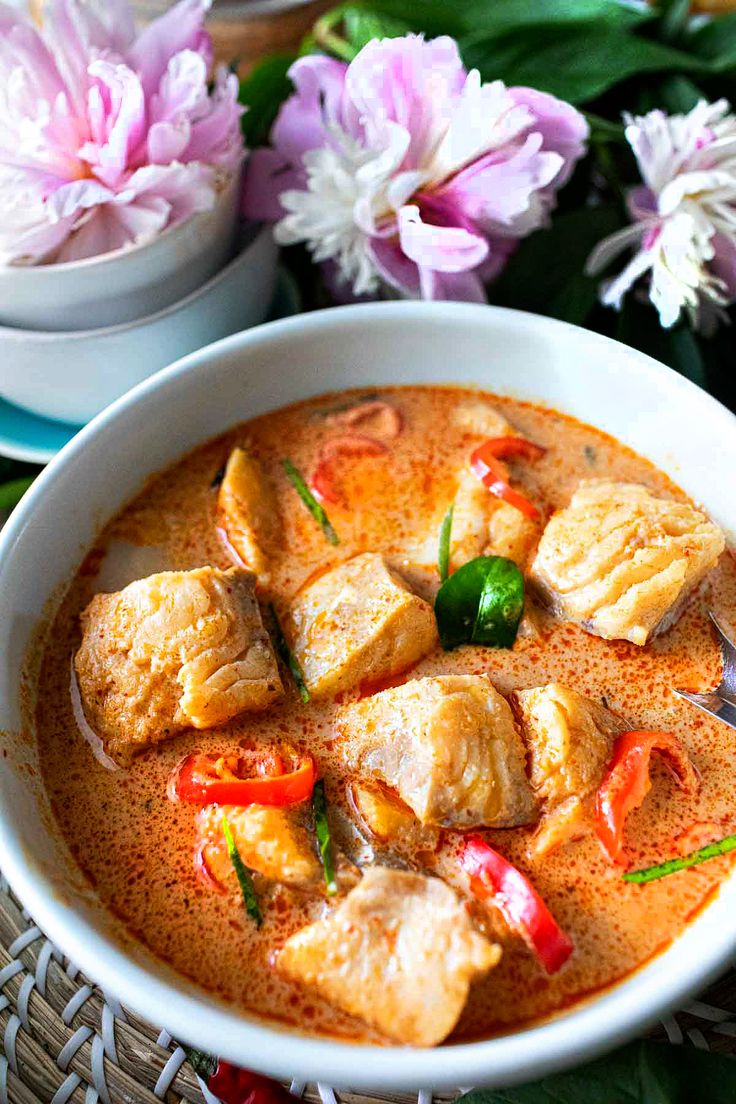 there is a bowl of soup with meat and vegetables in it on the table next to some flowers