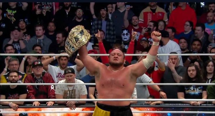 a man holding up a wrestling belt in front of a crowd with his arms raised