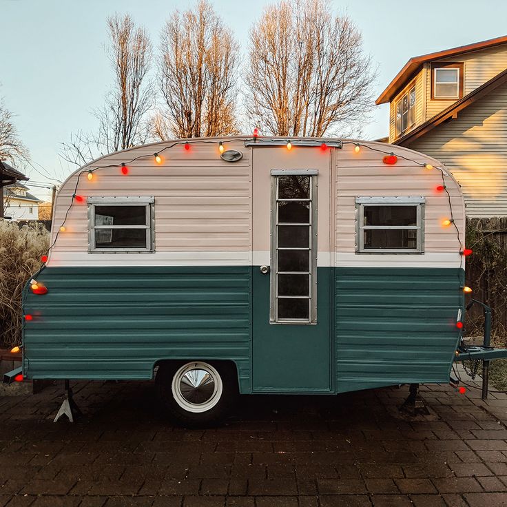 an old camper is parked in front of a house with christmas lights on the windows