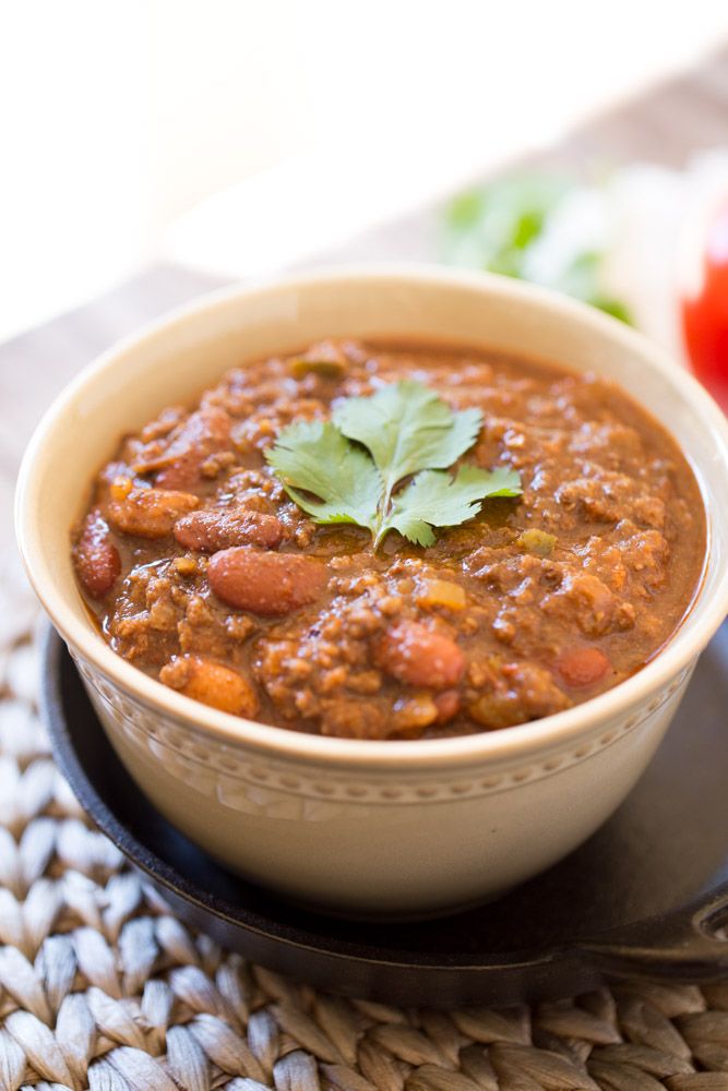 a bowl of chili on a plate next to some tomatoes and lettuce leaves