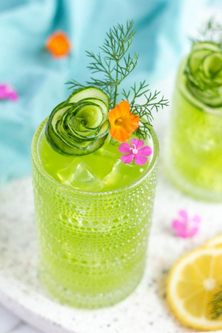 two glasses filled with lemonade and cucumber garnished with fresh flowers