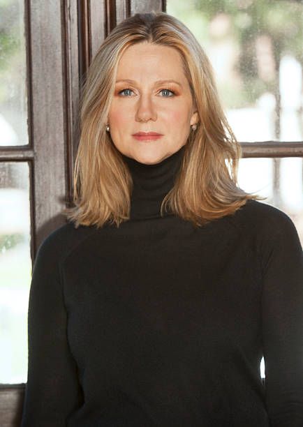 a woman standing in front of a window wearing a black turtle neck sweater and jeans